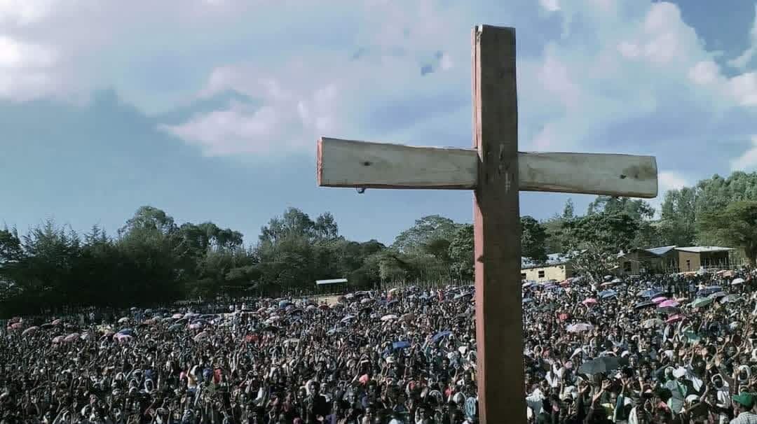 A wooden cross stands before a vast crowd gathered for a Gospel crusade