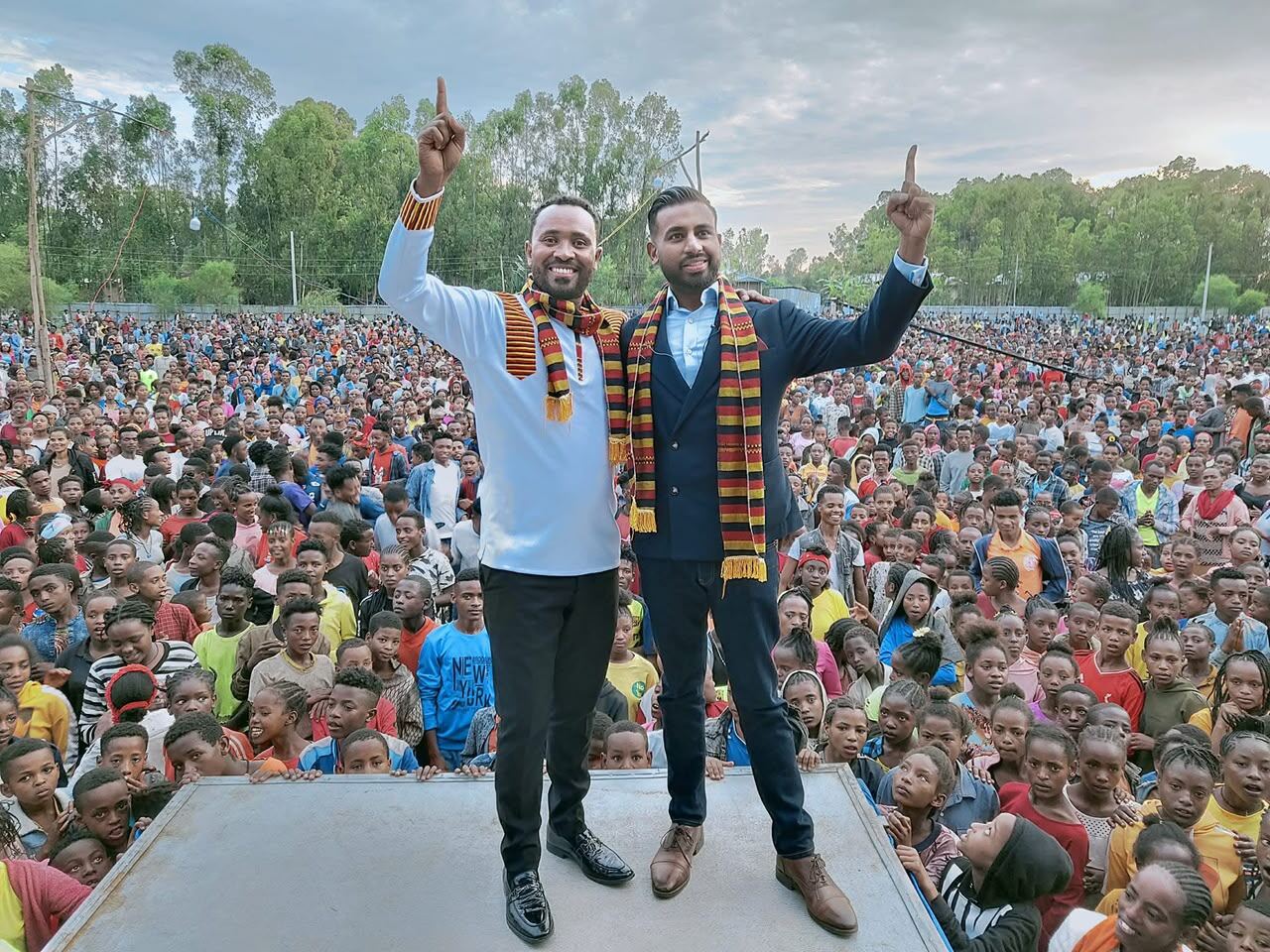 Evangelist Hailu Lemma with a partner minister, arms raised, before a crowd of young people